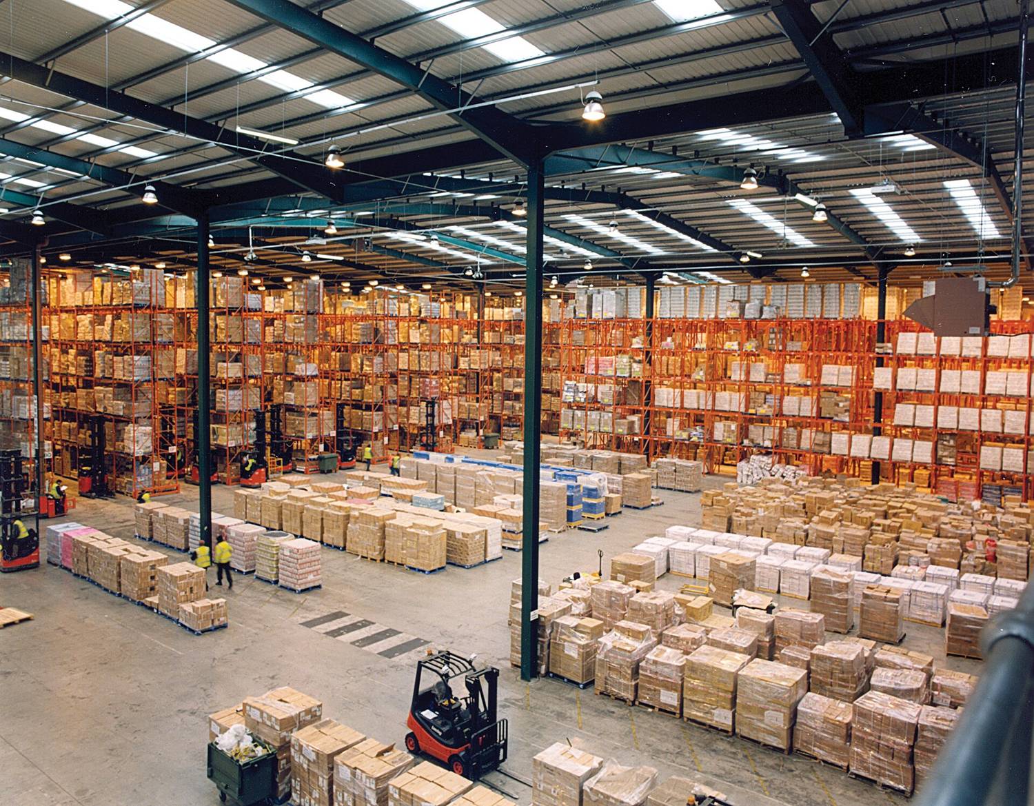 A wide warehouse floor lined with orange pallet racking